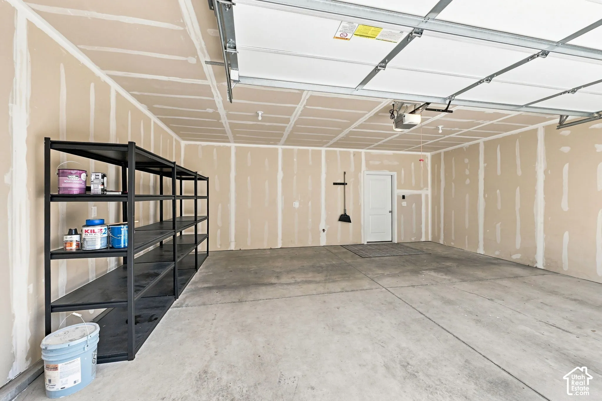 Concrete flooring, unfinished drywall, overhead garage door system, interior access door, wall-mounted storage rack