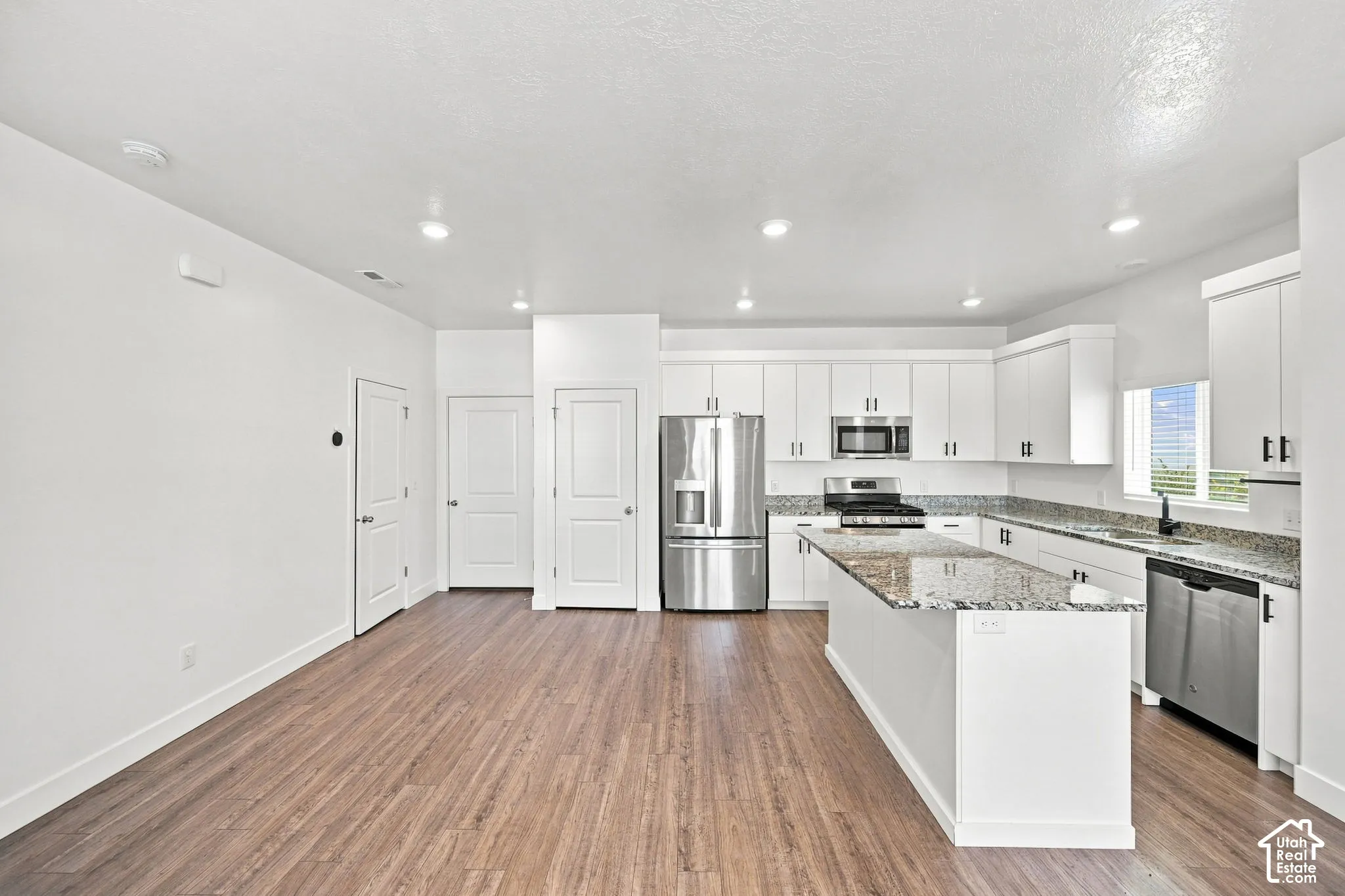 Modern kitchen featuring white cabinetry, stainless steel appliances, a center island with a granite countertop, and wood-finish flooring