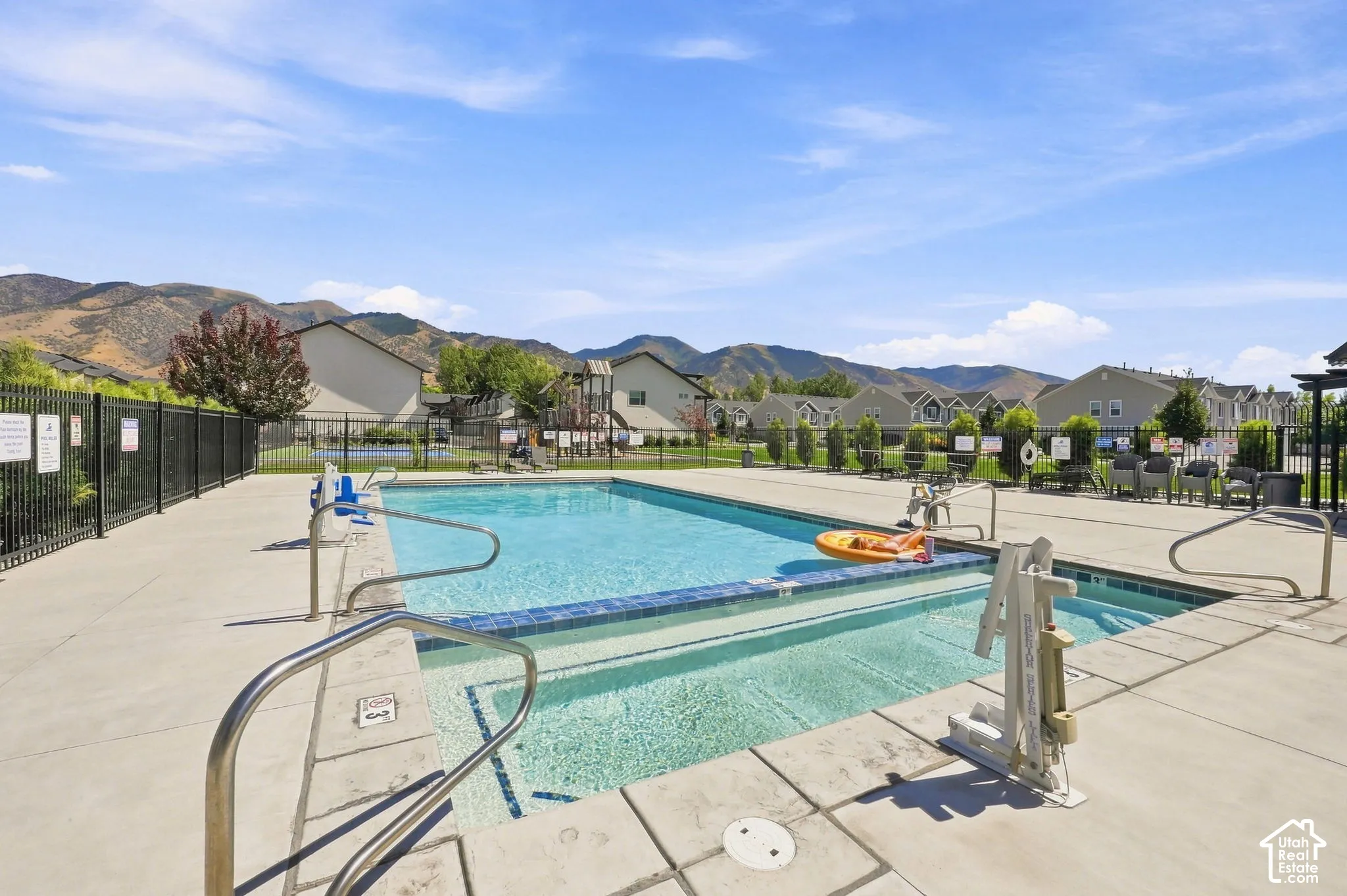 Community swimming pool with surrounding concrete decking, metal handrails, and a black perimeter fence