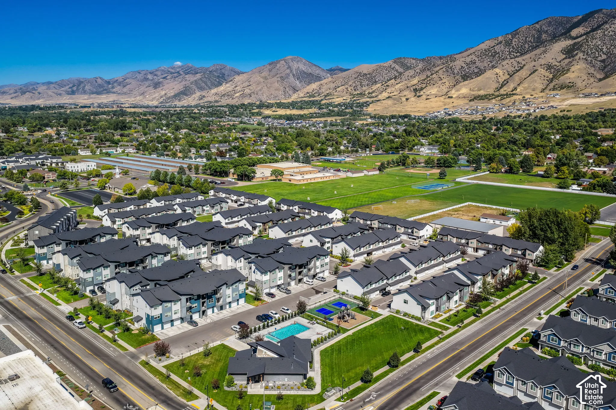 Expansive aerial perspective showcasing a residential development with a community pool, sports courts, and mountain scenery