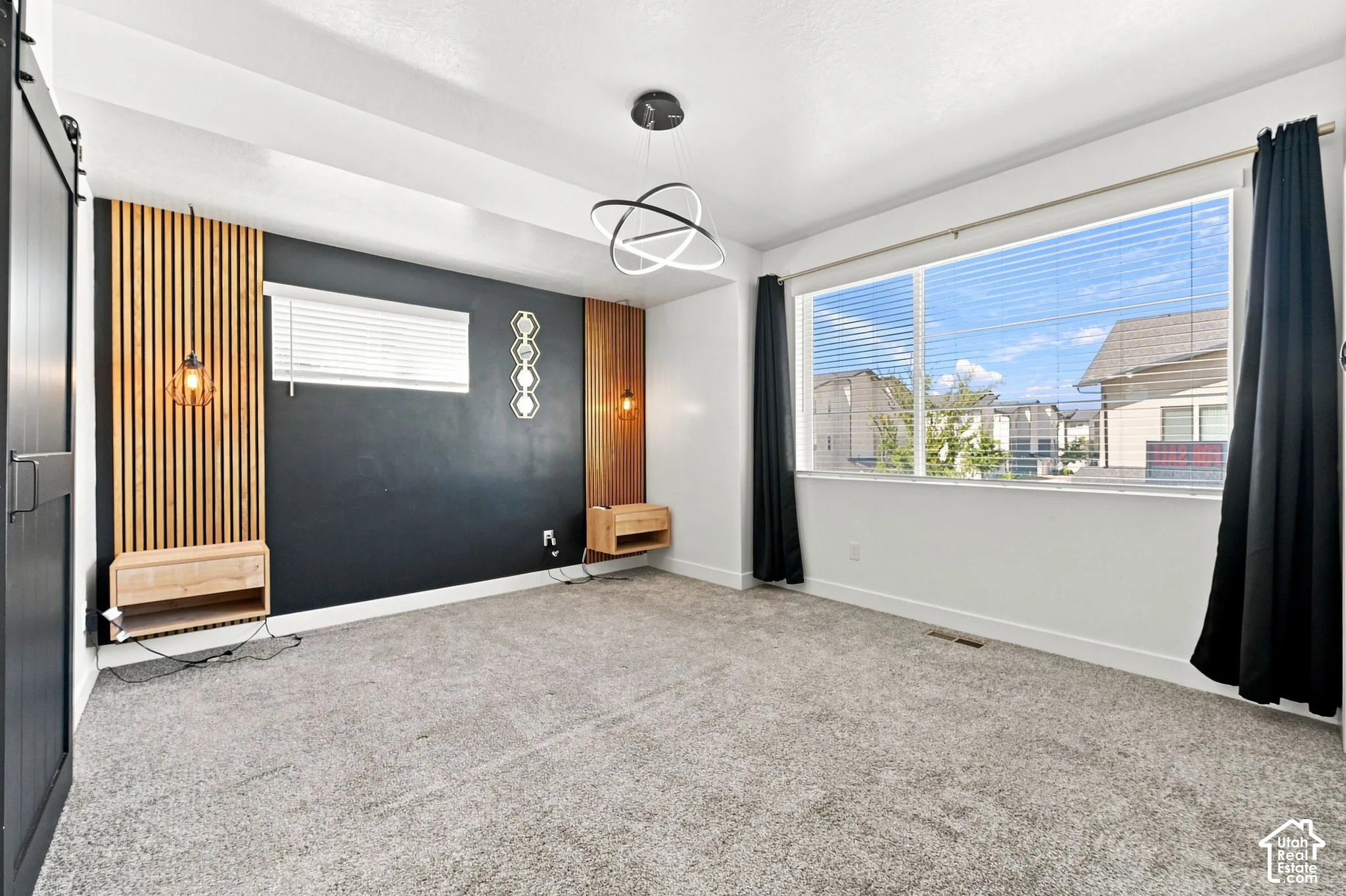 Wide window with blinds, wood-finish accent wall paneling, built-in floating nightstands, and a modern ceiling light fixture