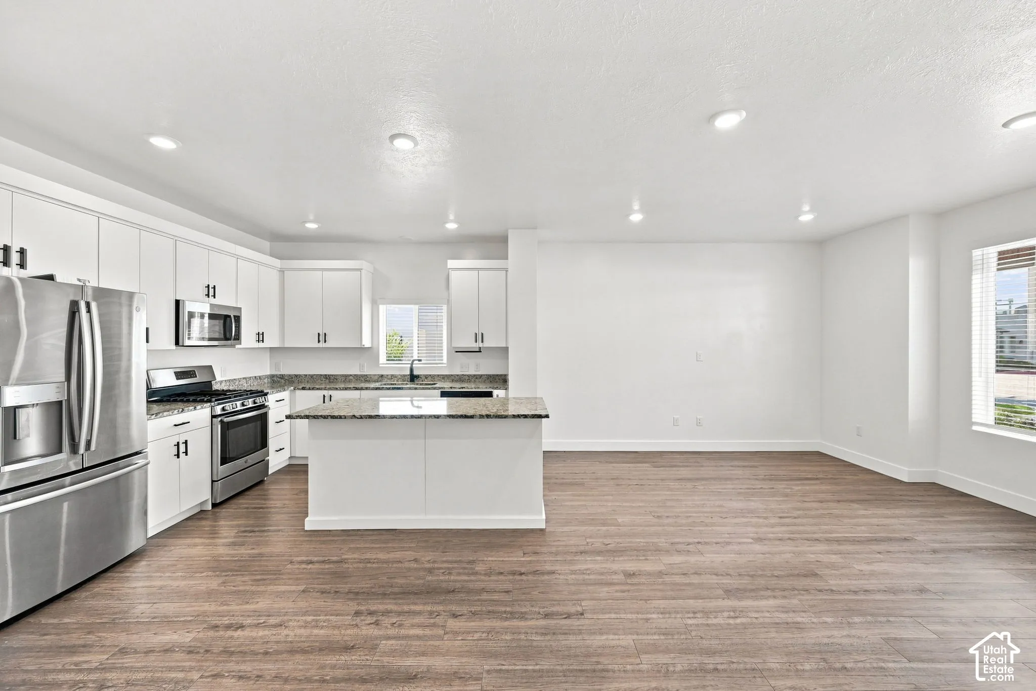 Modern kitchen featuring white cabinetry, stainless steel appliances, an island with a countertop, and wood-finish flooring