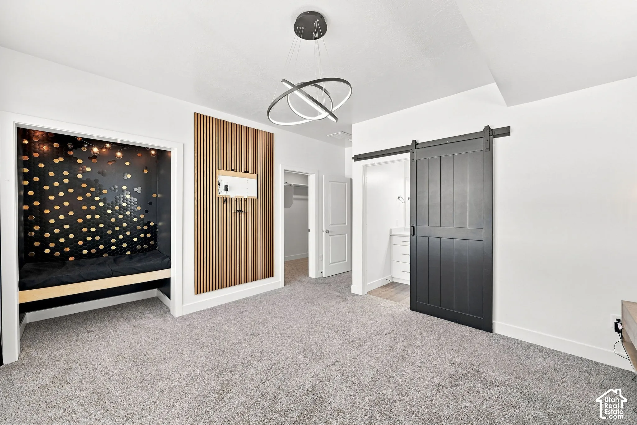 Built-in alcove seating, contemporary chandelier, slatted wood-finish wall accent, dark-tone barn door, and light gray carpeting