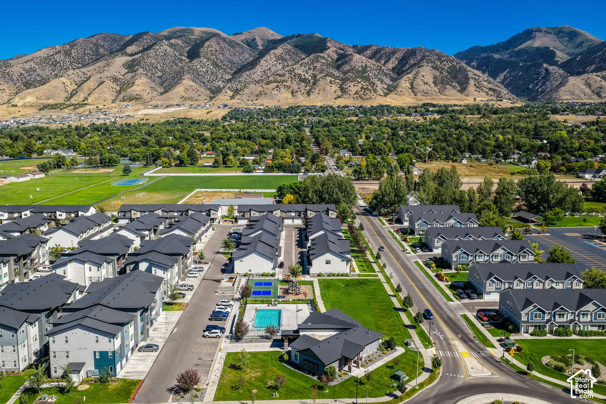 Community features multiple residential buildings with varied facades, a central swimming pool, and a sports court
