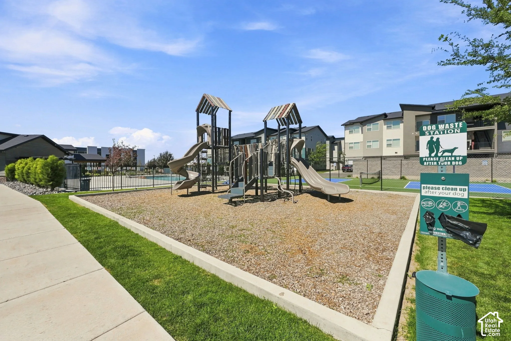 Playground area with slides and climbing structures, dog waste station, grassy areas, and paved walkways