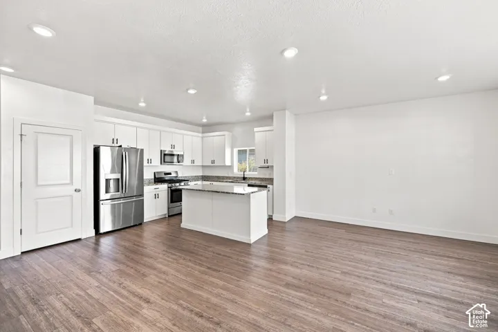 Open-concept living area with wood-finish flooring, recessed lighting, and a kitchen featuring white cabinetry, stainless steel appliances, and a central island with a countertop