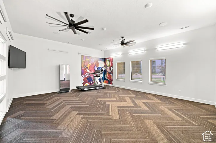 Spacious room featuring patterned flooring, multiple windows, two ceiling fans, and wall-mounted lighting