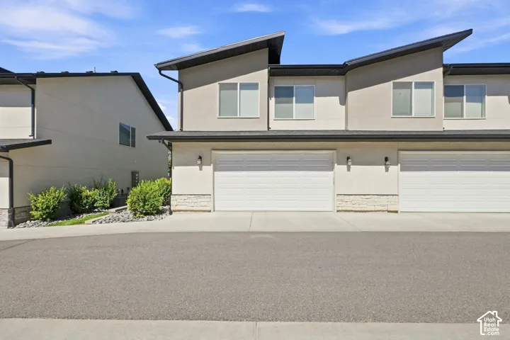 Contemporary exterior with stucco siding, white garage doors, and a stone accent facade