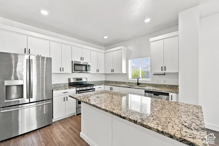 Kitchen with white cabinetry, stainless steel appliances, granite countertops, an island, and wood-finish flooring