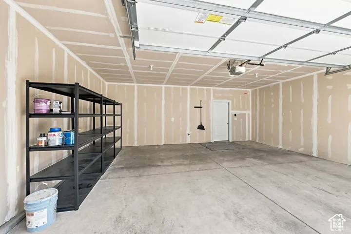 Concrete flooring, unfinished drywall, overhead garage door system, interior access door, wall-mounted storage rack