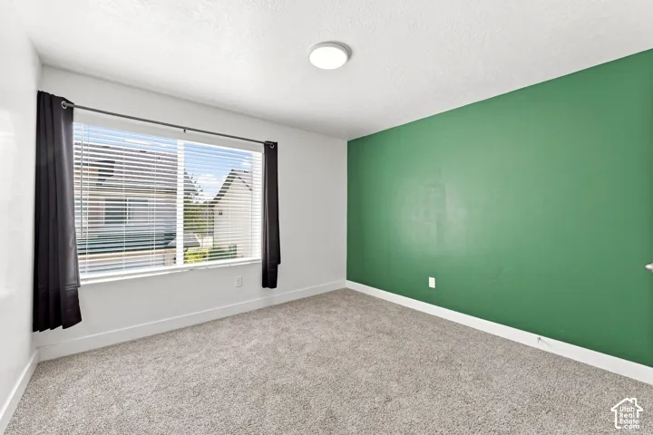 Neutral carpeted flooring, large window with blinds, recessed ceiling light, and a prominent accent wall