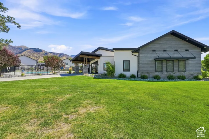 Expansive green space, modern exterior design, covered entryway with wood columns, fenced pool area, and mountain backdrop