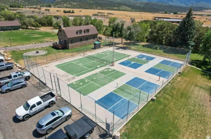 Multiple outdoor courts with fencing, paved parking area, and surrounding green space
