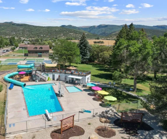 Outdoor swimming pool with water slide, adjacent tennis courts, and surrounding natural landscape