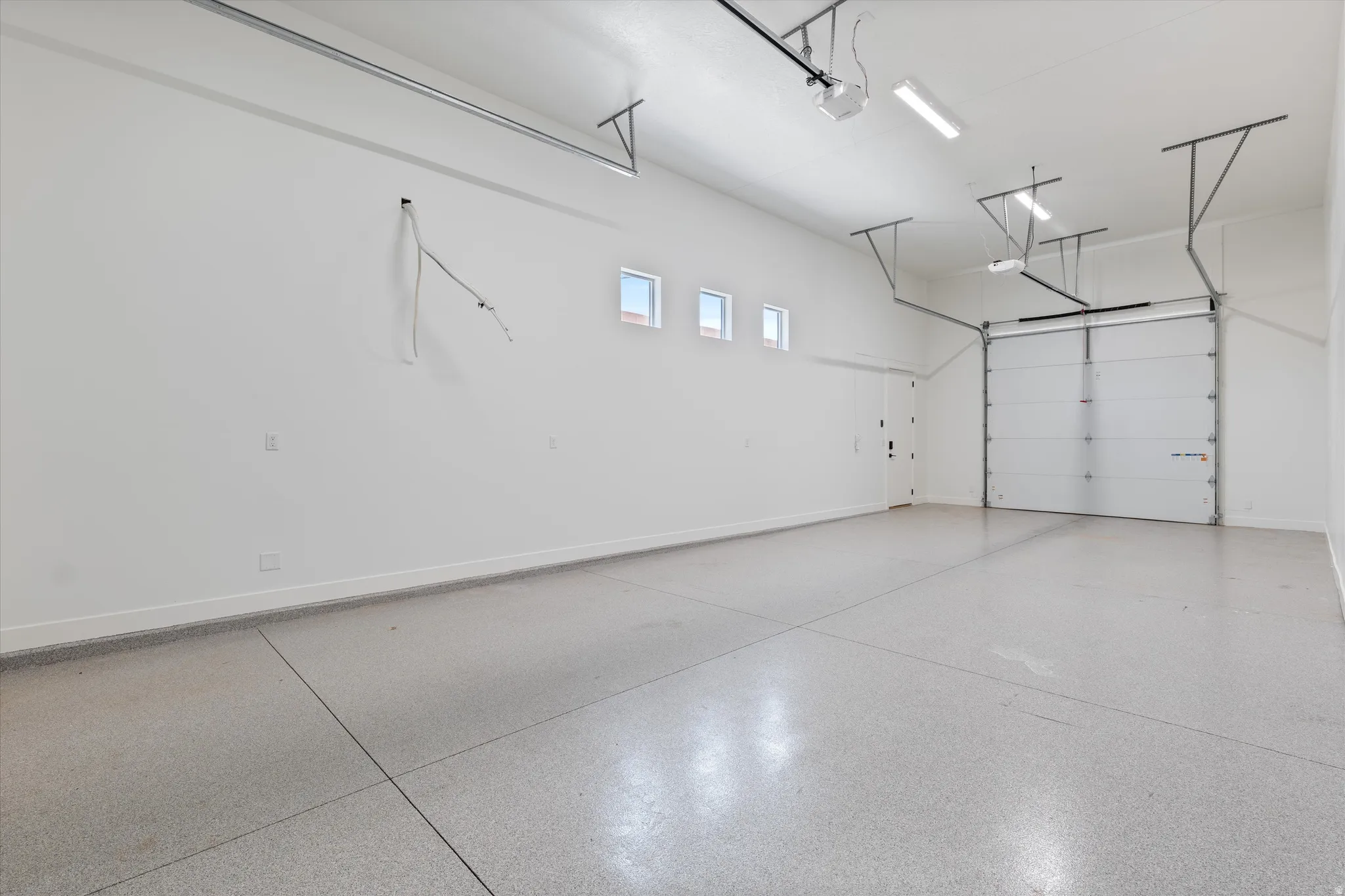 Spacious garage featuring a durable epoxy floor, white walls, multiple windows, and overhead lighting