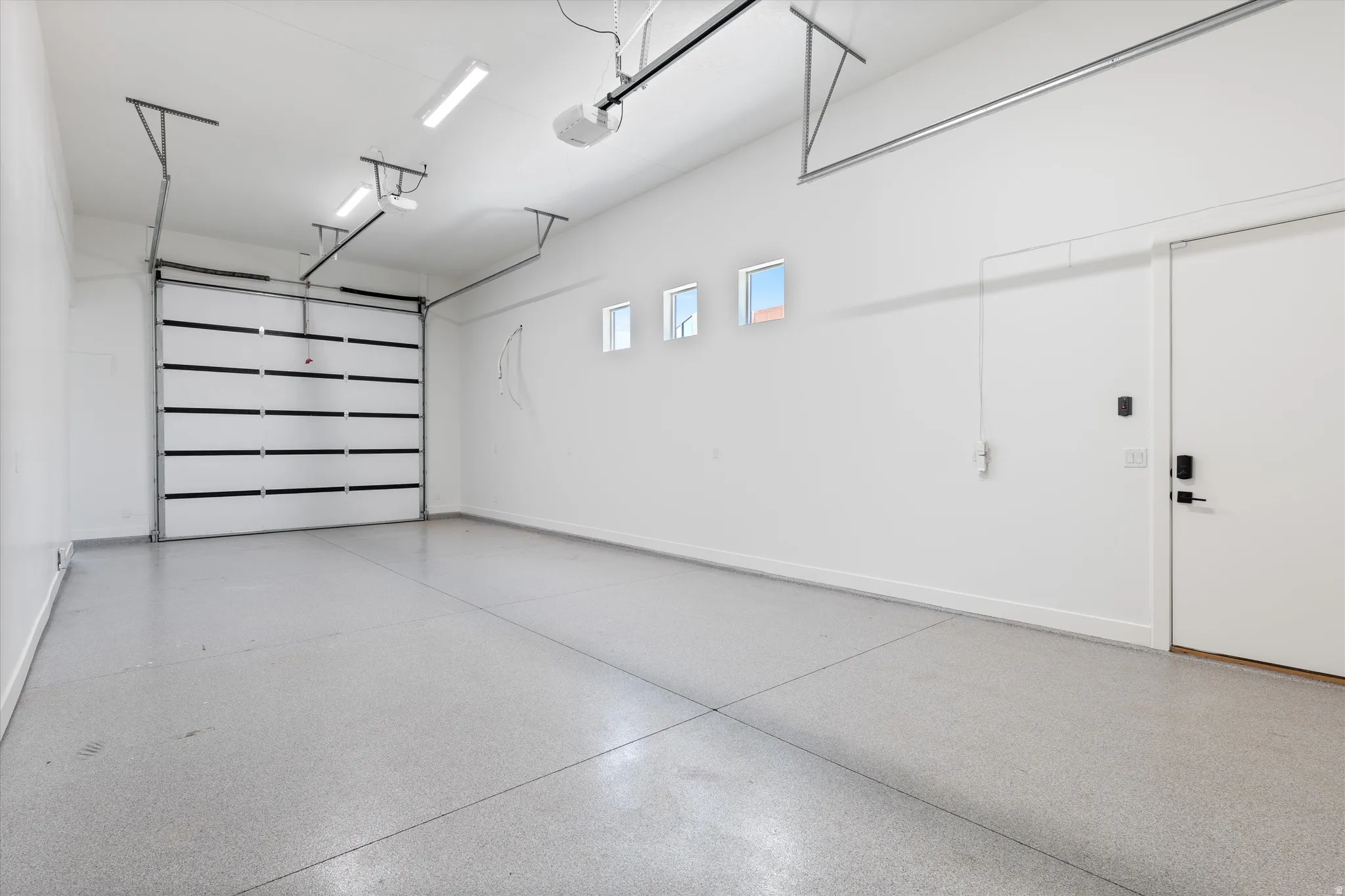 Two-car garage with a sectional overhead door, three transom windows, a side access door, and an epoxy-coated concrete floor