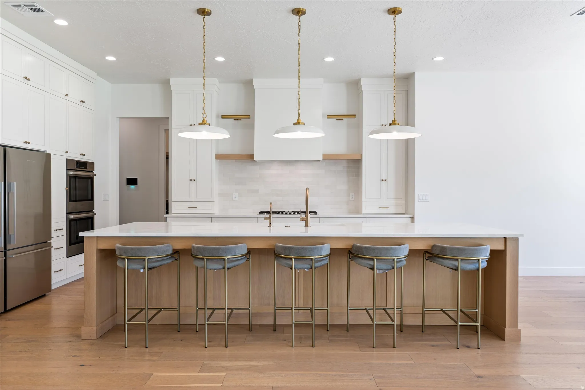 Expansive kitchen island with a light-toned wood finish, solid surface countertop, and three pendant lights