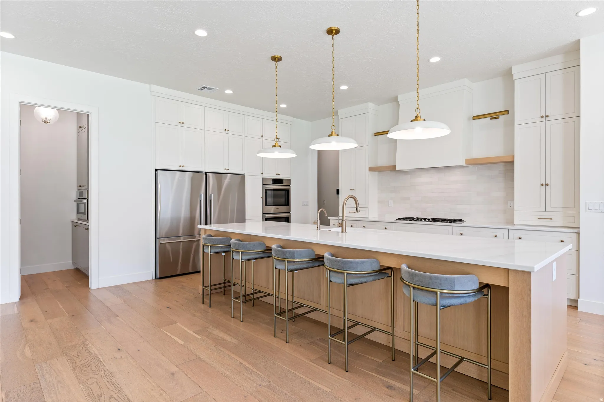 Spacious kitchen featuring light wood-finish flooring, a large island with seating, stainless steel appliances, white cabinetry, and recessed lighting