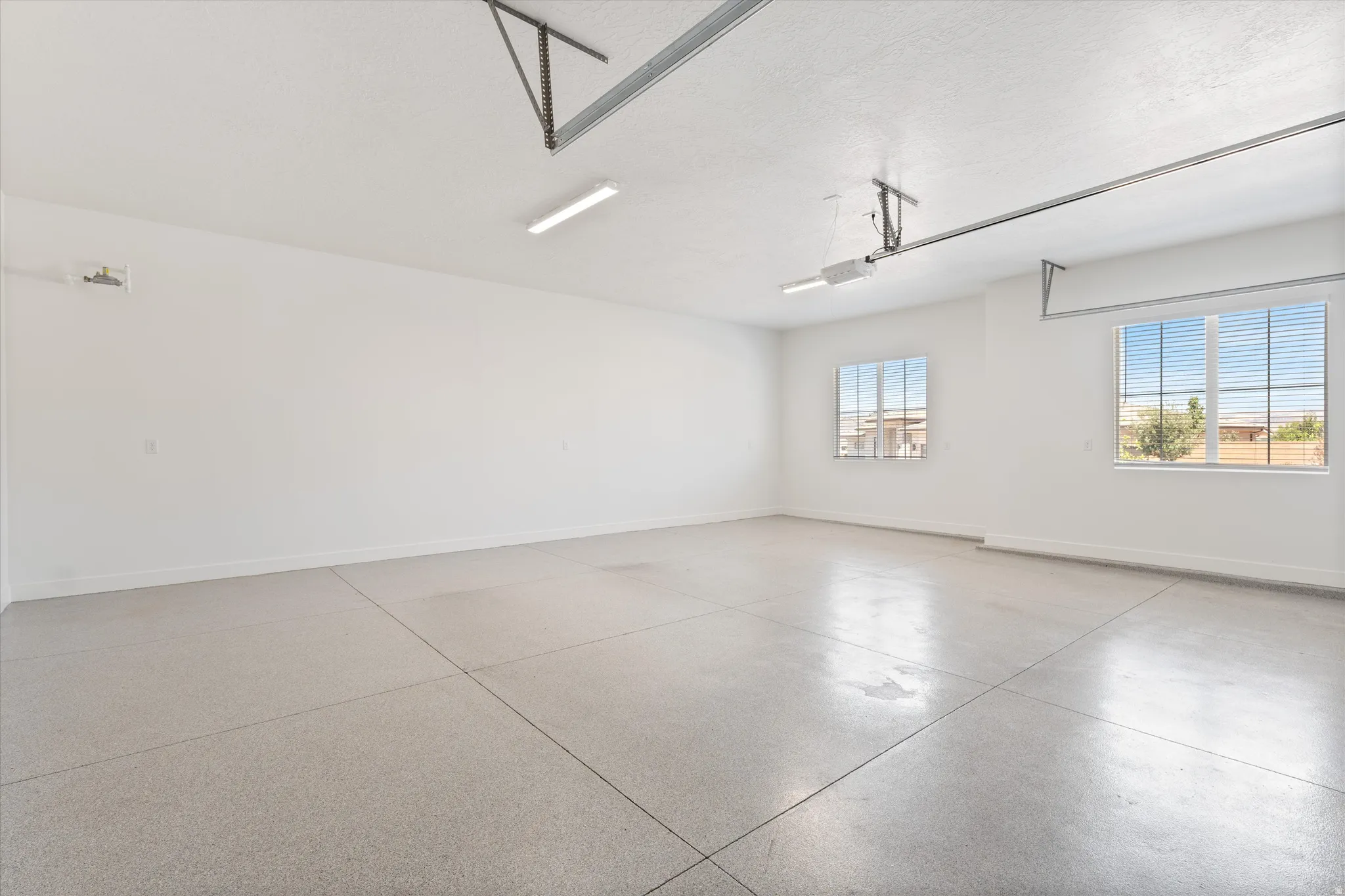 Spacious garage featuring a finished floor, two windows with blinds, and overhead lighting