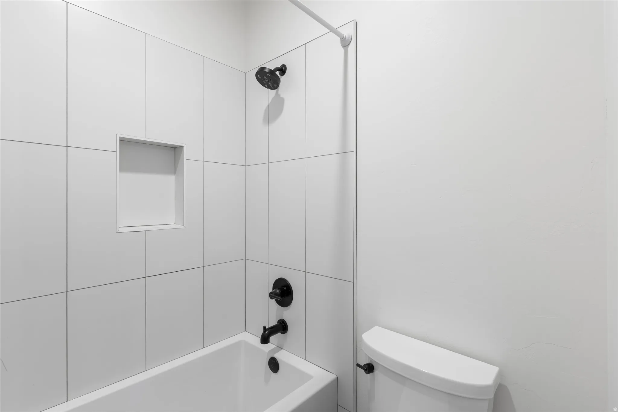 White tiled shower with a built-in niche, black shower fixtures, and a white bathtub
