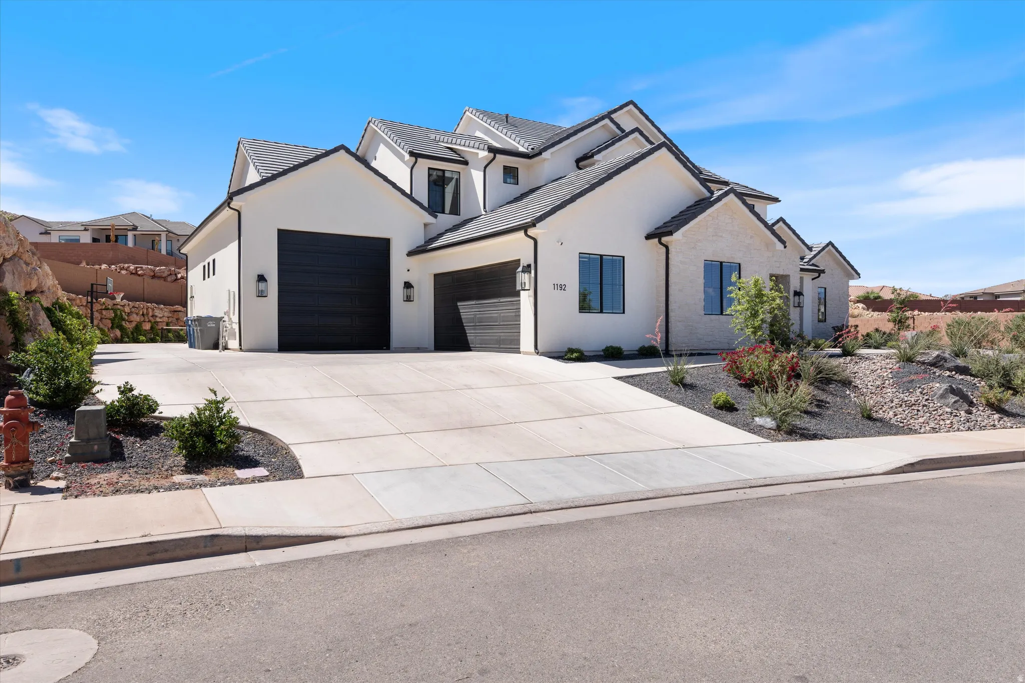 Contemporary residence featuring a white stucco and stone exterior, multi-gabled roofline, black-framed windows, and a wide concrete driveway