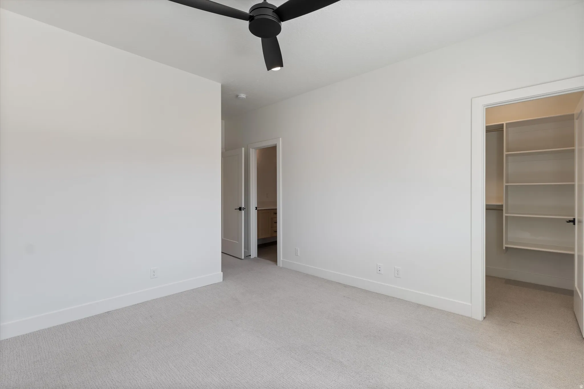 Carpeted flooring, white walls, black ceiling fan, built-in closet shelving, and white interior doors