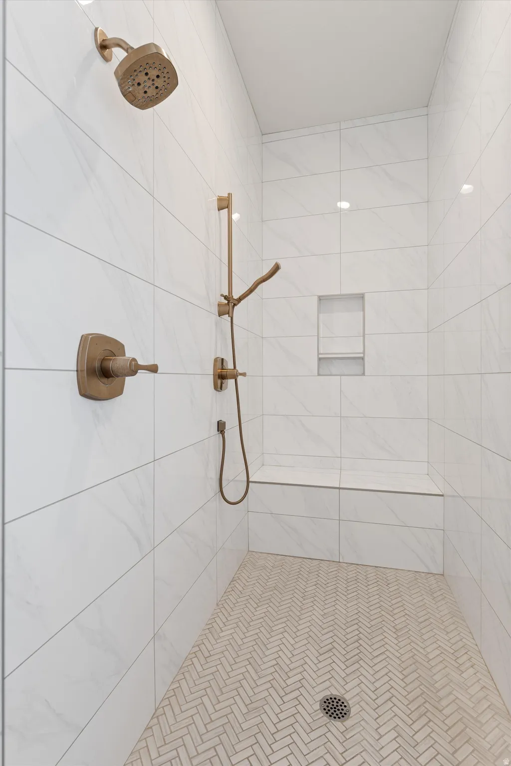 Walk-in shower with large format wall tiling, integrated shower bench, herringbone pattern floor tiling, and a recessed shower niche