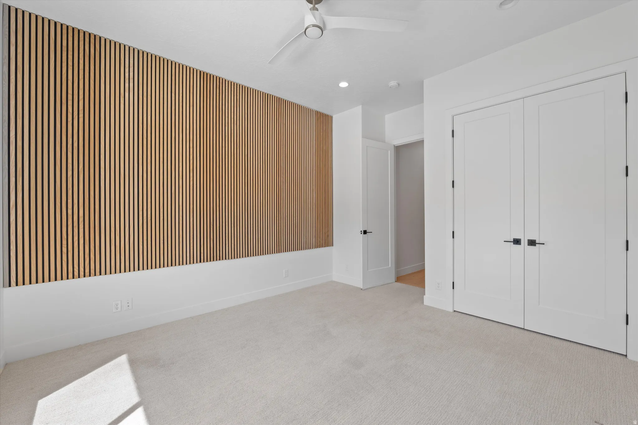 Accent wall with vertical wood paneling, recessed lighting, ceiling fan, and carpeted flooring