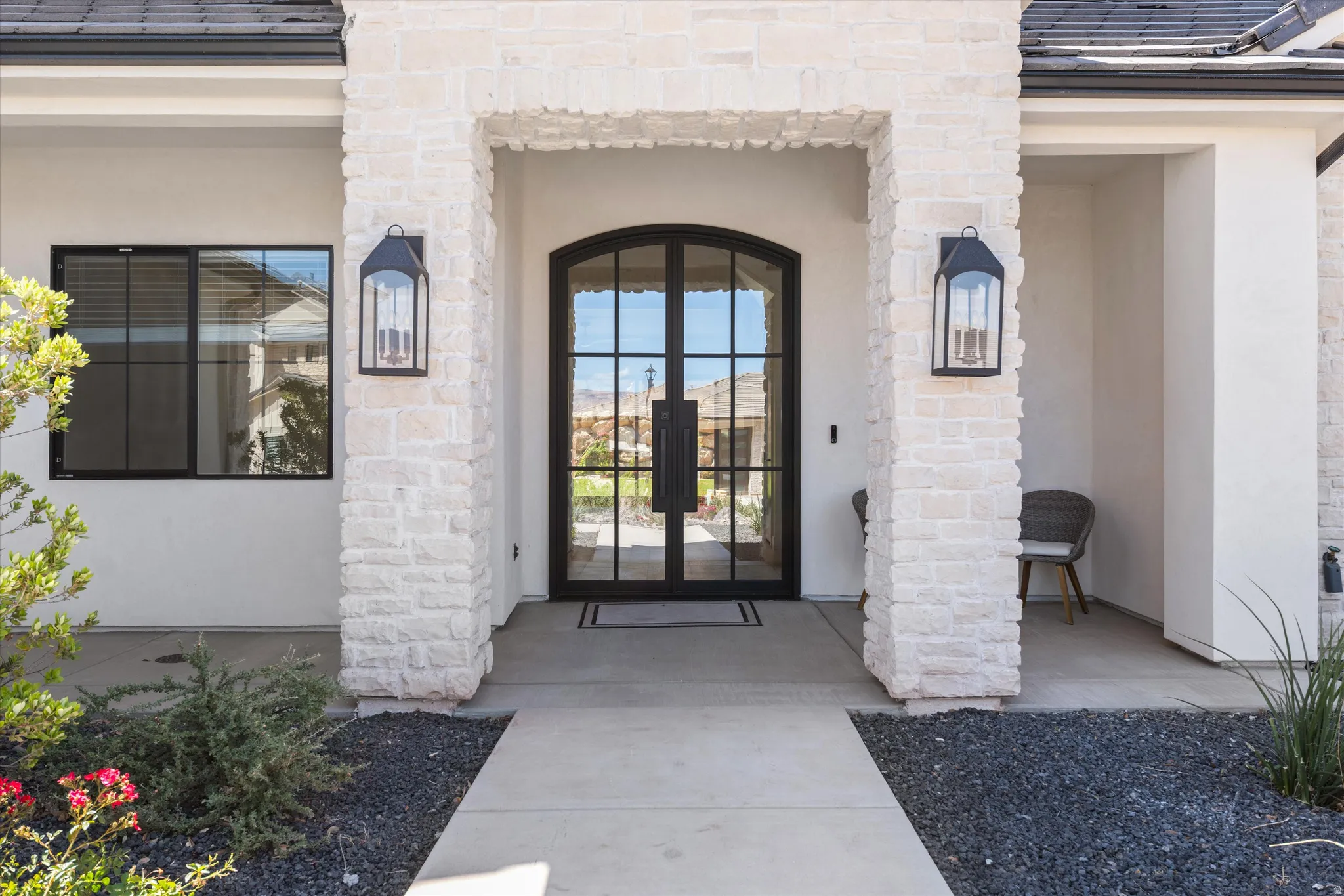 Stone facade entrance featuring a double arched iron door, exterior sconces, and a concrete pathway