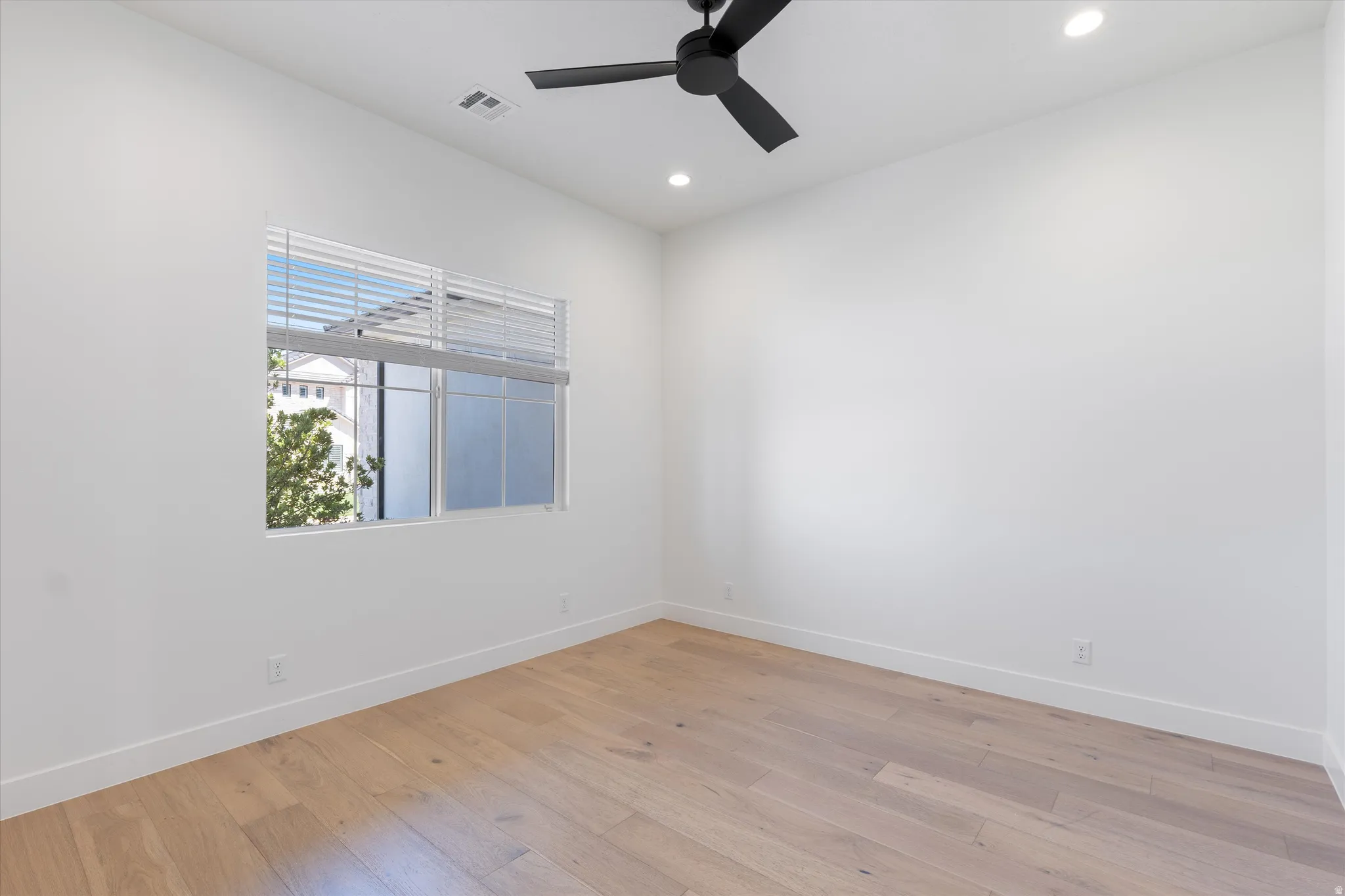 Recessed lighting, wood-finish flooring, white walls, black ceiling fan, and a single window