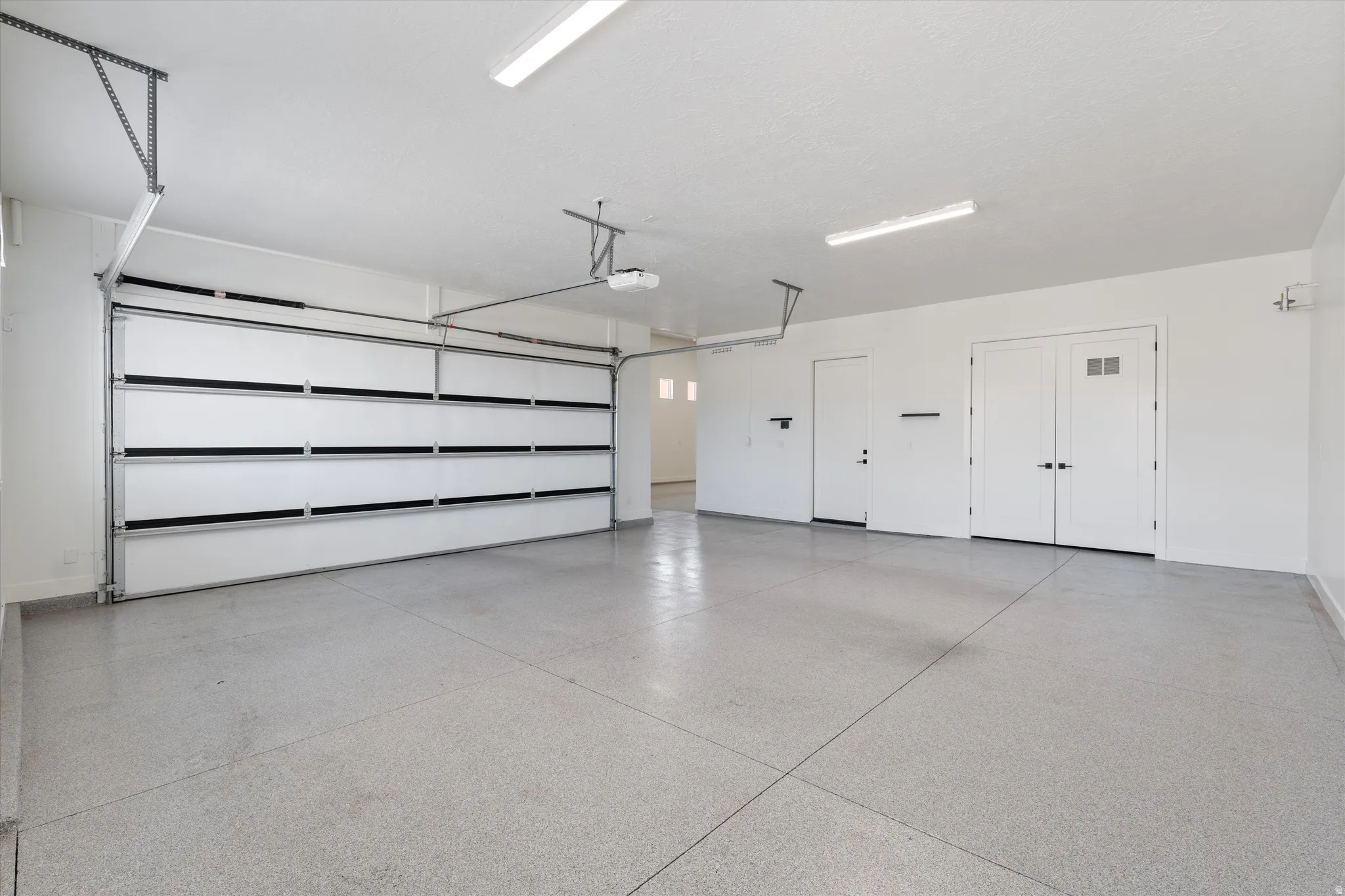 Spacious garage featuring a durable epoxy floor, white sectional garage door, recessed lighting, and a double entry door with glass inserts