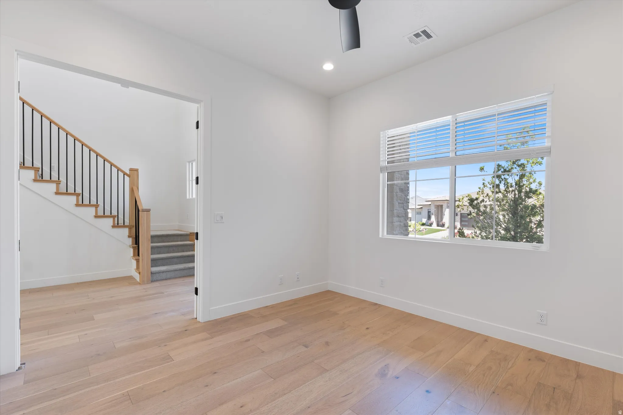 Recessed lighting, wood-finish flooring, staircase with wood-finish handrail and black metal spindles, ceiling fan, and large window with blinds