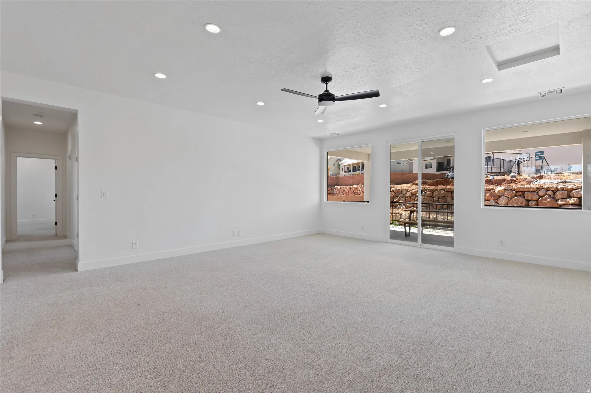Recessed lighting, ceiling fan, white walls, light-colored carpet, and sliding glass door