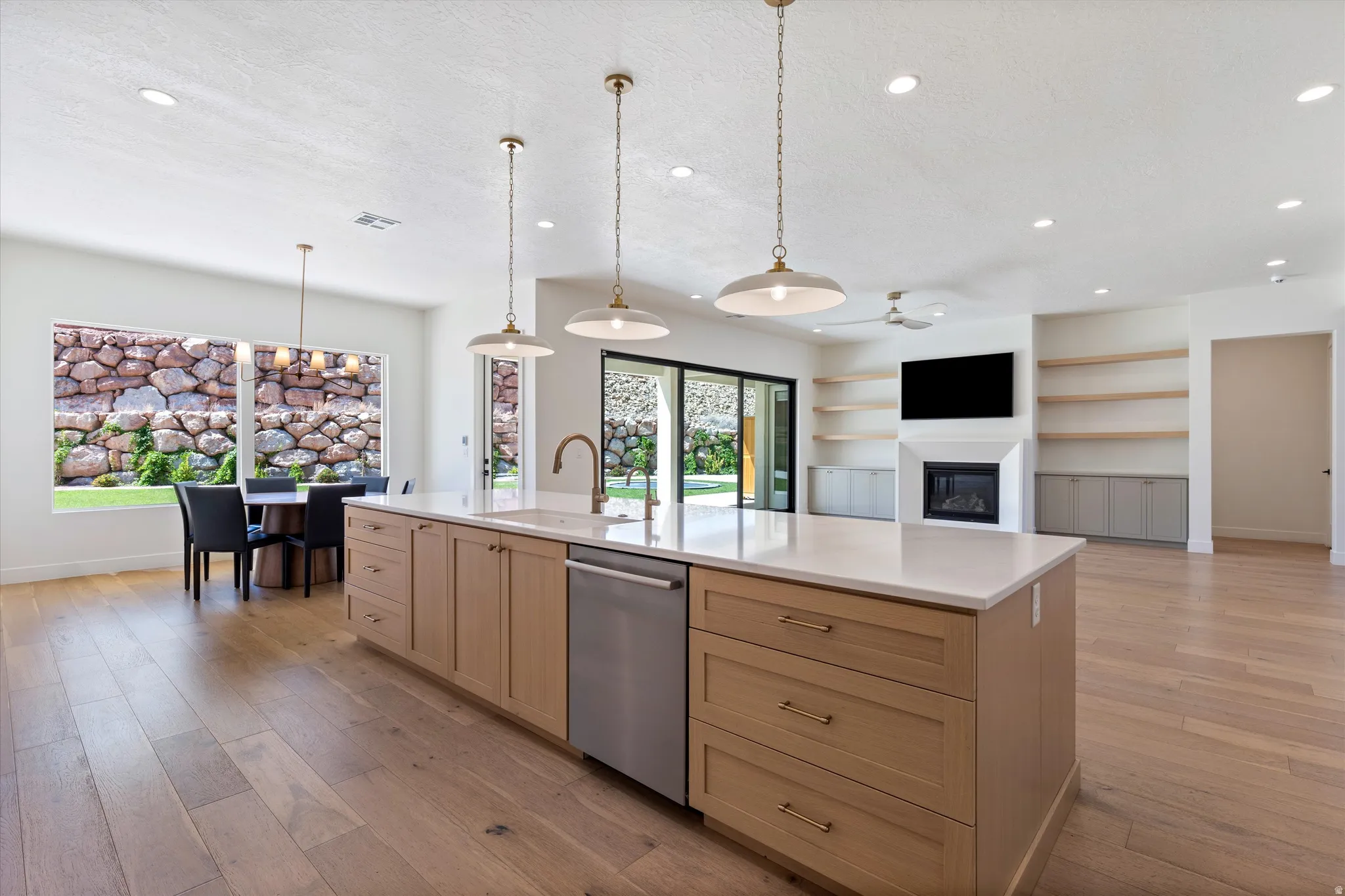 Open-concept interior with wood-finish flooring, a kitchen island with light cabinetry and a light-toned countertop, and a fireplace with built-in shelving