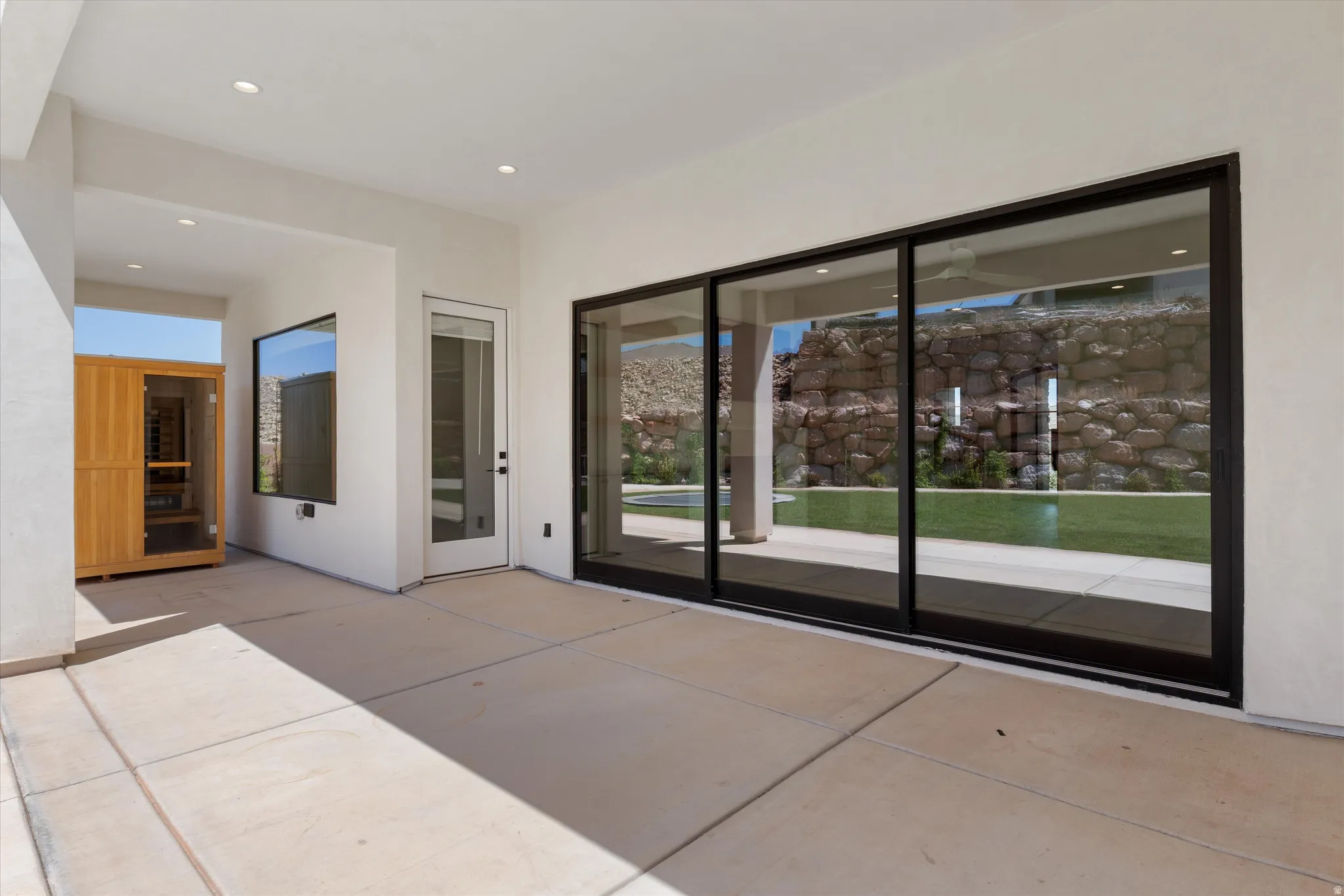 Covered patio featuring concrete flooring, a built-in sauna, and black-framed sliding glass doors