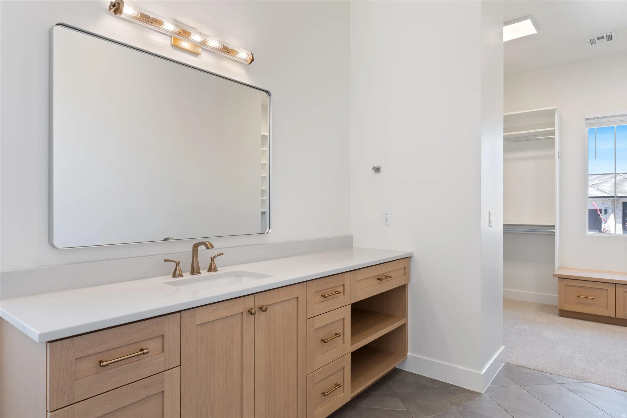 Wood-finish vanity with a rectangular undermount sink, a bronze-finish faucet, and a large rectangular mirror