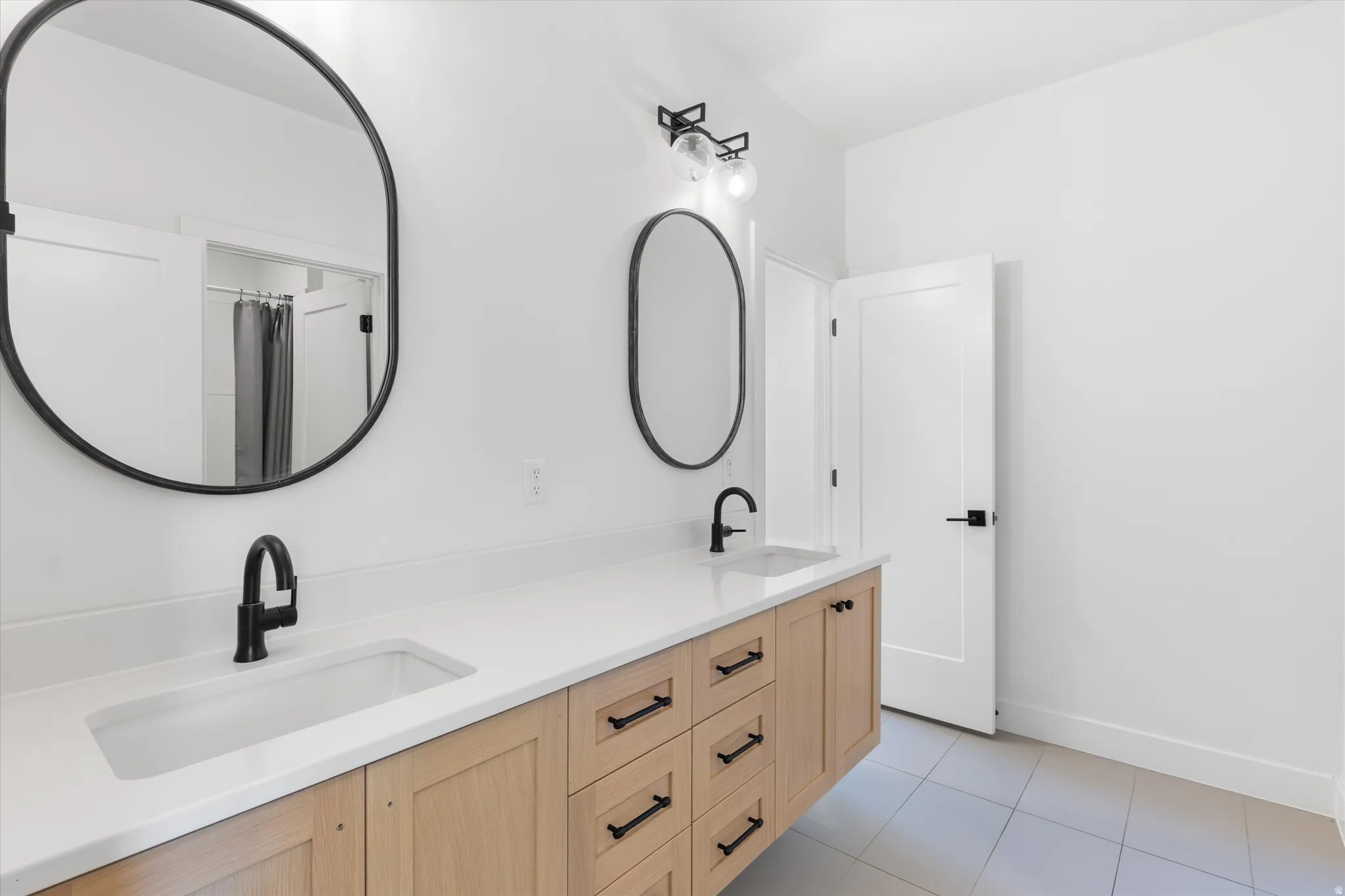 Dual vanity with wood-finish cabinetry, white countertop, and matte black fixtures