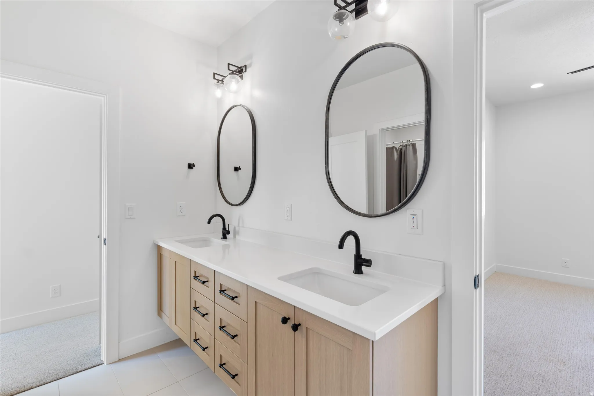 Double vanity with light wood-finish cabinetry, white countertops, and matte black fixtures