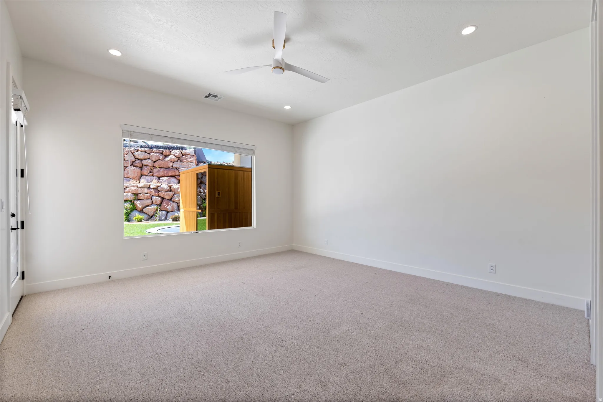 Recessed lighting, ceiling fan, neutral carpeting, white walls, and a window with outdoor scenery