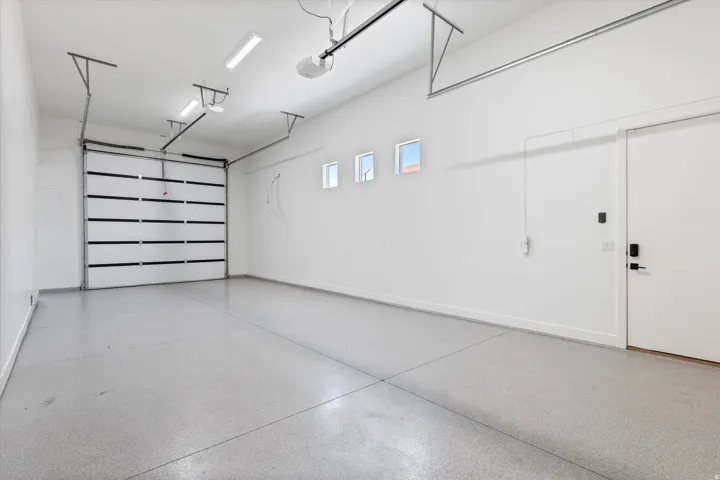 Two-car garage with a sectional overhead door, three transom windows, a side access door, and an epoxy-coated concrete floor