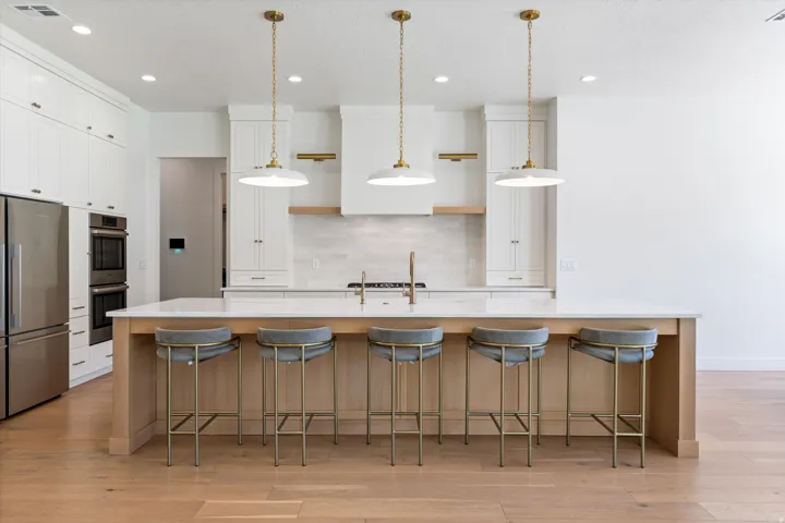 Expansive kitchen island with a light-toned wood finish, solid surface countertop, and three pendant lights