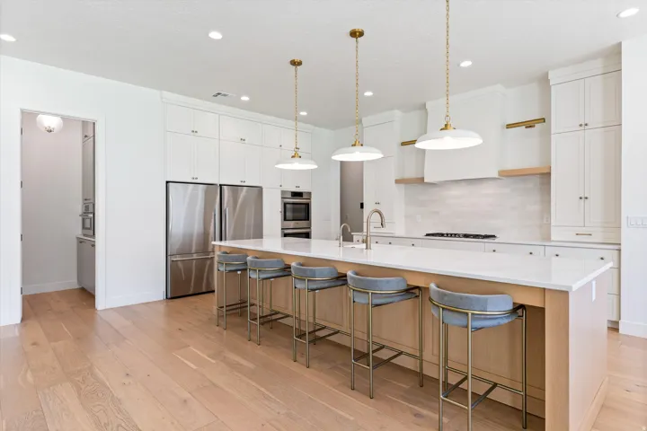 Spacious kitchen featuring light wood-finish flooring, a large island with seating, stainless steel appliances, white cabinetry, and recessed lighting