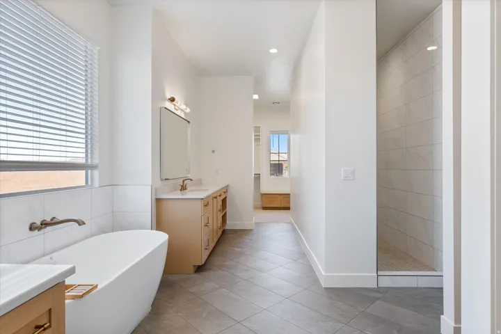 Freestanding soaking tub with wall-mounted bronze-finish faucet, dual vanity with undermount sinks, bronze-finish hardware, and a walk-in shower with tiled walls and flooring