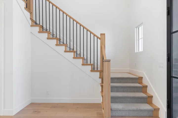 Natural wood staircase with black iron balusters, light wood-finish flooring, and a window providing natural light