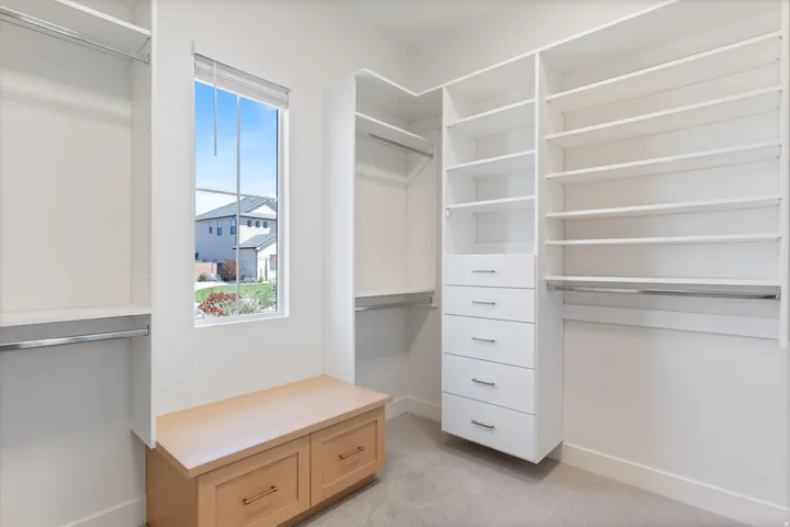 White built-in shelving, integrated drawers with metal pulls, chrome hanging rods, and a light wood-finish storage bench with drawers