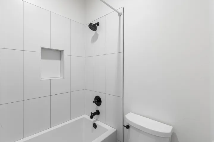 White tiled shower with a built-in niche, black shower fixtures, and a white bathtub