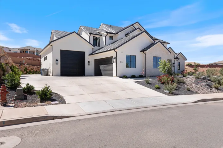 Contemporary residence featuring a white stucco and stone exterior, multi-gabled roofline, black-framed windows, and a wide concrete driveway