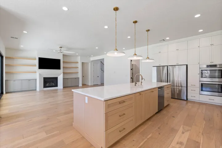 Expansive open concept living area featuring wood-finish flooring, a kitchen island with pendant lighting, stainless steel appliances, and a fireplace with built-in shelving