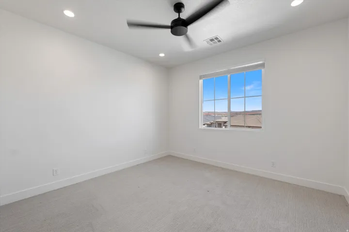 Recessed ceiling lighting, ceiling-mounted fan, large window, and light-toned carpeting