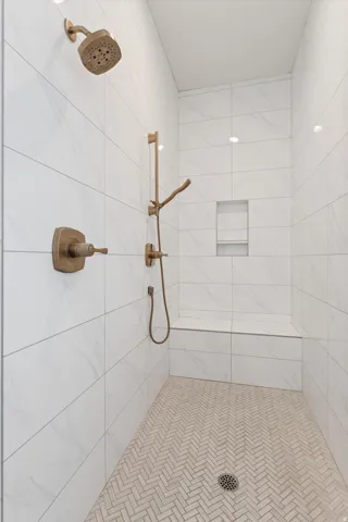 Walk-in shower with large format wall tiling, integrated shower bench, herringbone pattern floor tiling, and a recessed shower niche
